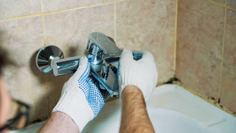 las manos con guantes del fontanero instalan el grifo en el baño.