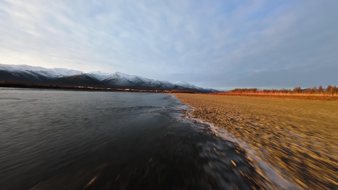 Experience the stunning beauty of Yakutia from above, where the vast river meets snow-capped mountains under the expansive sky. Nature’s grandeur unfolds in each sweeping view.