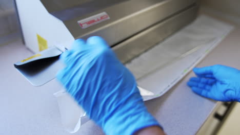 female medic in blue latex gloves places long metal tool into a plastic bag. nurse prepares instrument for sterilization in modern equipment.
