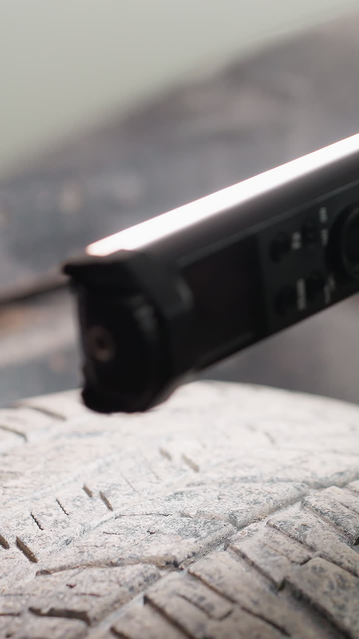 Primo piano di un pneumatico d'auto ispezionato con una torcia LED luminosa in un'officina meccanica, evidenziando i dettagli del battistrada e il controllo di manutenzione per usura, danni e condizioni generali.