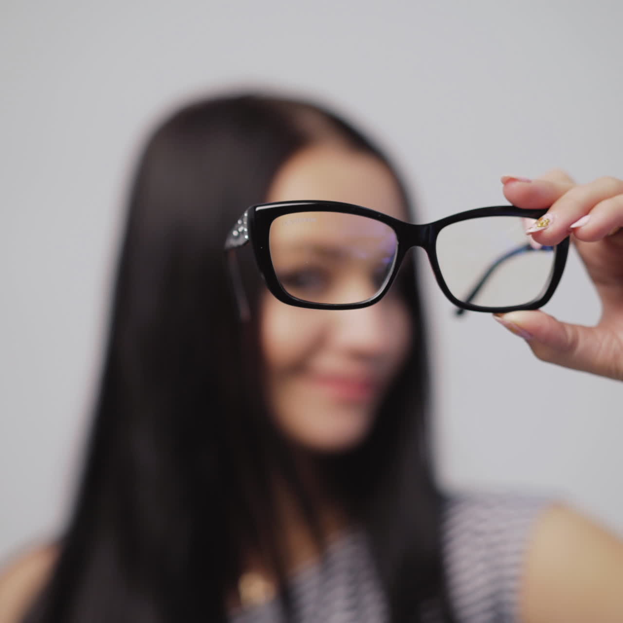 Pretty woman shows from left to right stylish eyeglasses and puts them on with blur background. Fashionable glasses in the hand of dark-haired female. Close-up