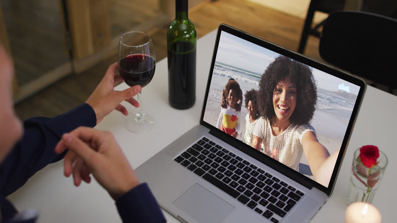 Mulher afro-americana bebendo vinho durante uma videochamada no notebook em casa