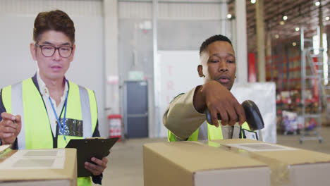 diverse male workers wearing safety suits and scanning boxes in warehouse