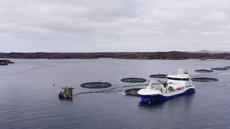 descending drone shot of a well-boat anchored beside a fish farming pen