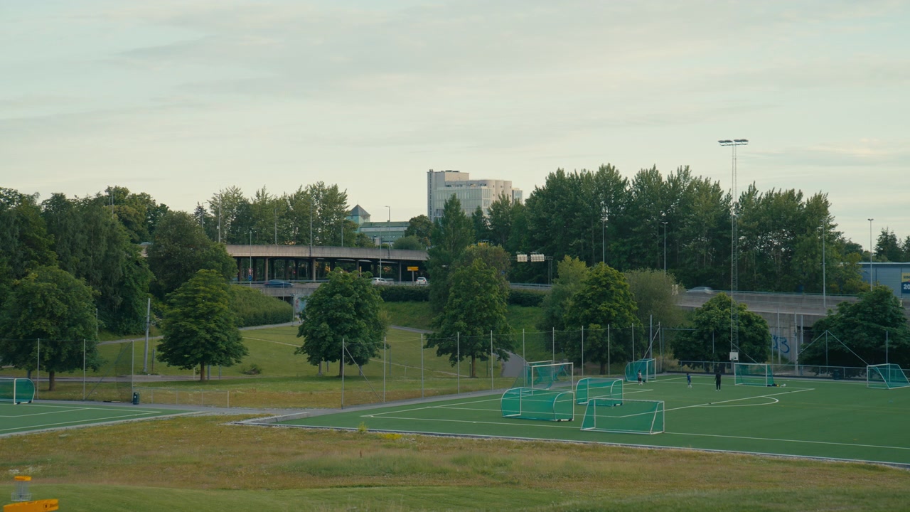 Et breddefotballanlegg i Oslo, Norge, ligger ved siden av veier, trær og lave bygårder, og fanger den daglige rammen for ungdomstrening, lokal veiledning og utvikling i akademistil