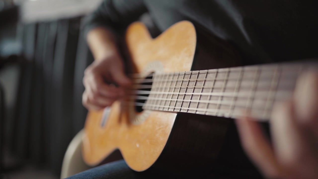 Primo piano delle mani che strimpellano una chitarra acustica, creando un'atmosfera calma e creativa.