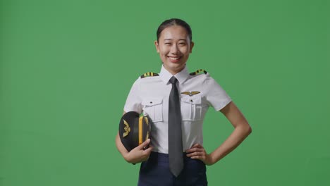 asian woman pilot with arms akimbo looking at camera and smiling while standing in the green screen background studio