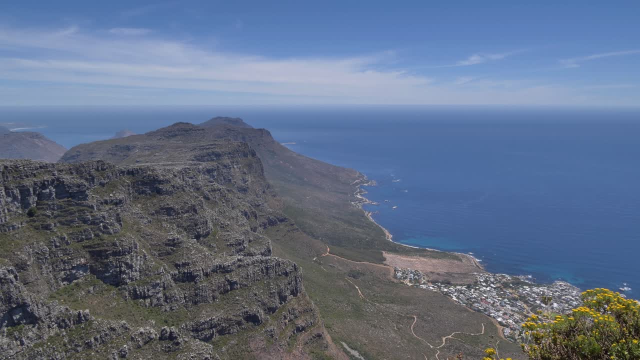 Una prospettiva aerea mozzafiato mostra Camps Bay situata tra le spettacolari scogliere della catena montuosa dei Dodici Apostoli e il vasto oceano blu sotto un cielo sereno, Sudafrica