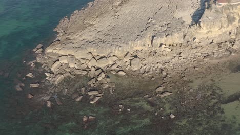 Aerial,-drone-shot,-over-the-sea,-towards-surfers-on-the-lighthouse-of-Sao-Pedro-do-Estoril,-on-a-calm,-sunny-day,-in-Lisbon,-Portugal