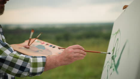 a skilled craftsman is captured in the midst of his creative process, holding a paint palette in one hand and a brush in the other as he gently applies green paint to a large white canvas