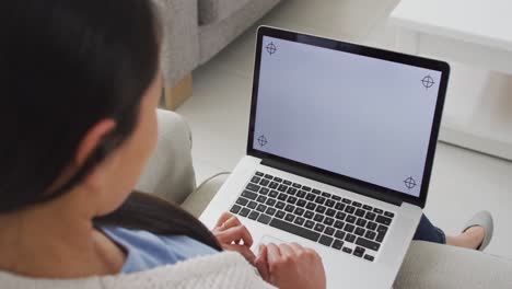 vista posterior de una mujer asiática sentada en el sofá, descansando con una computadora portátil con espacio de copia en casa