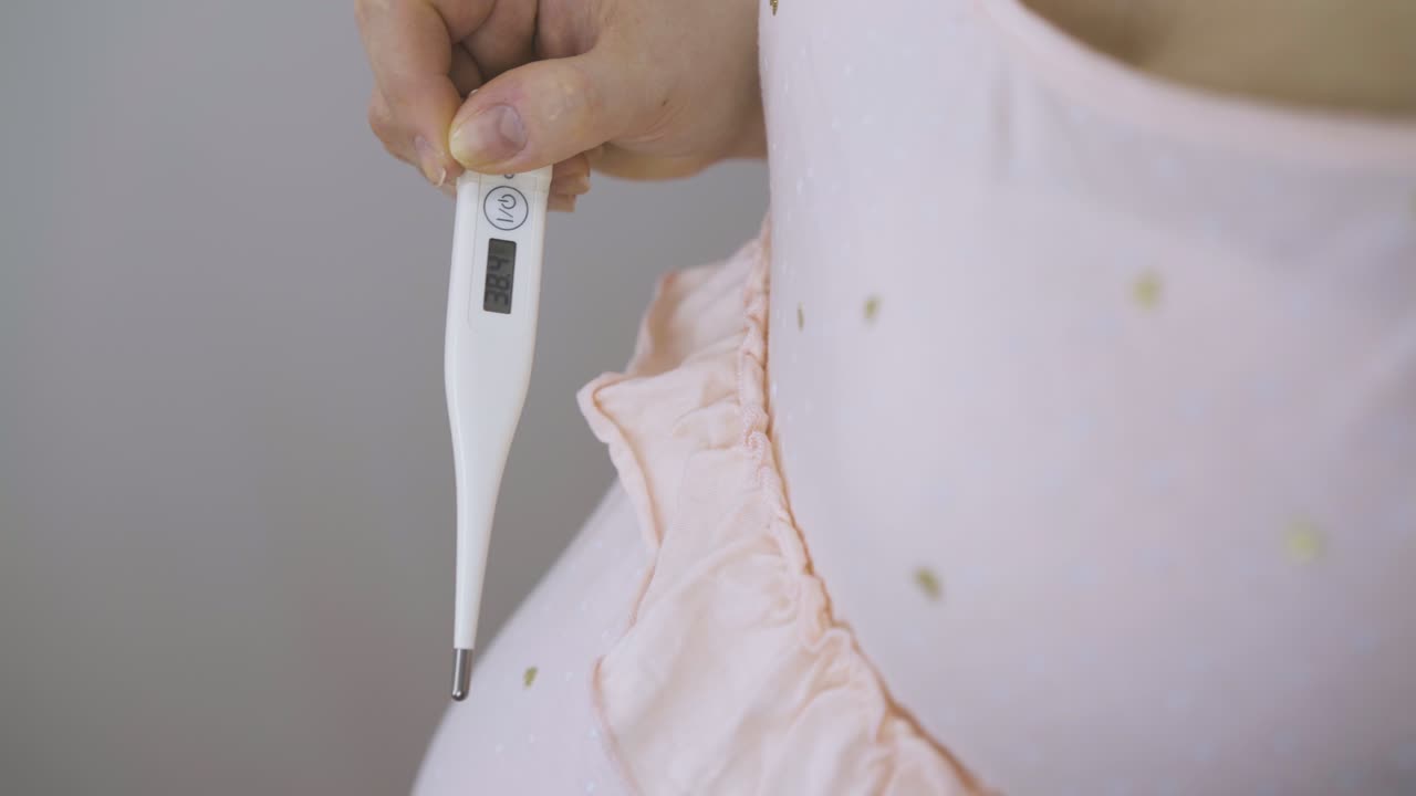 임신 한 여자 는 디지털 온도계 를 들고 배 를  ⁇ 는다