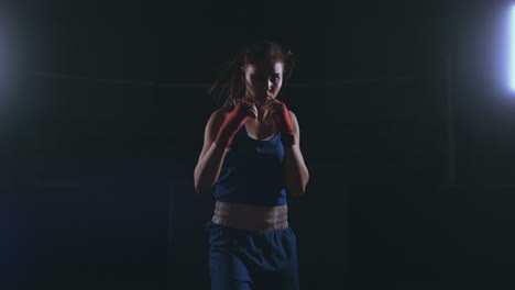 Looking-into-the-camera-a-beautiful-female-boxer-strikes-against-a-dark-background-with-a-backlit-light.-Steadicam-shot