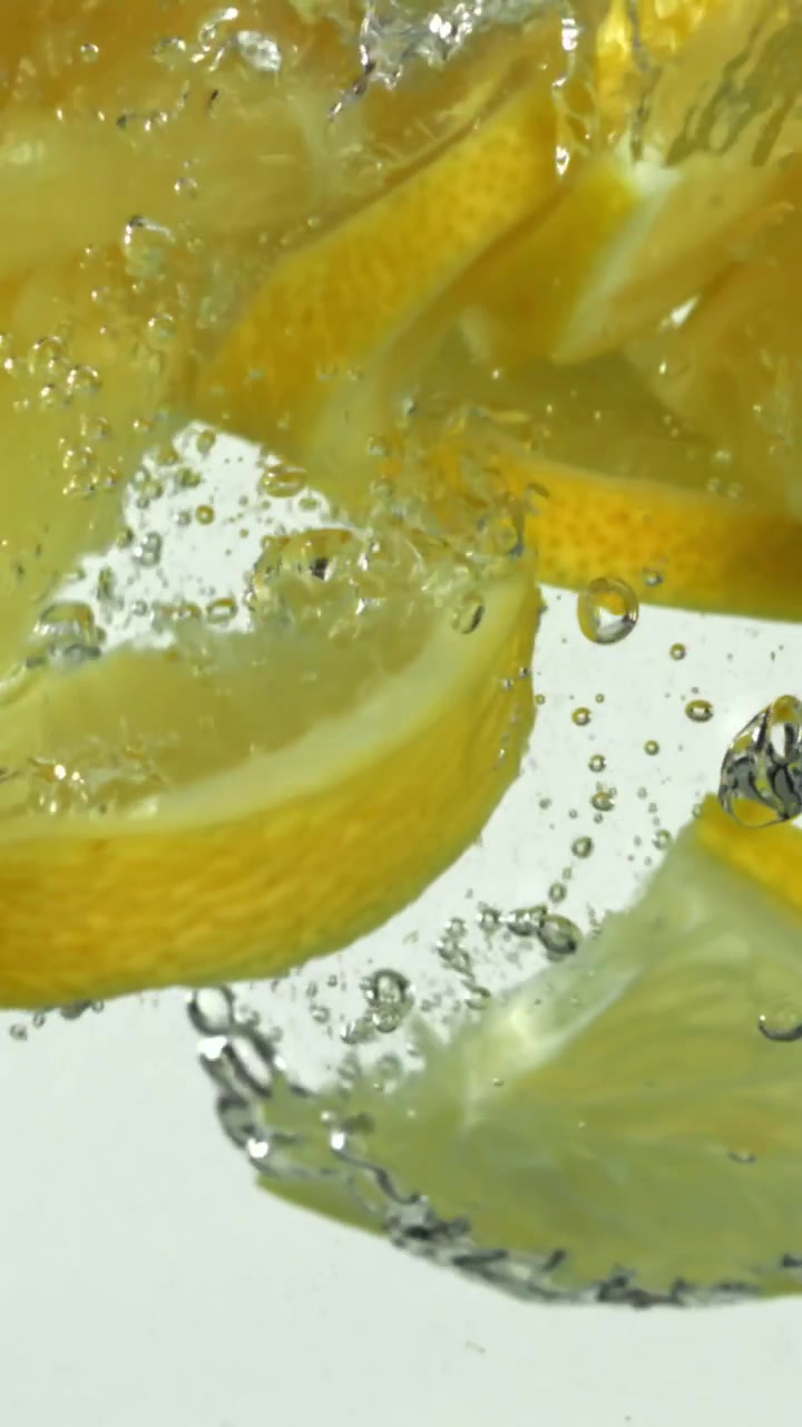 Fette di limone fresche che si tuffano nell'acqua con bolle