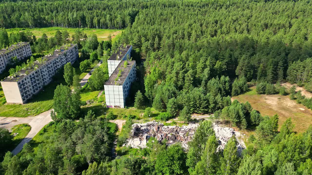 Вид с дрона на заброшенные бетонные здания, утопающие в пышном зеленом лесу, с руинами и заросшими сооружениями