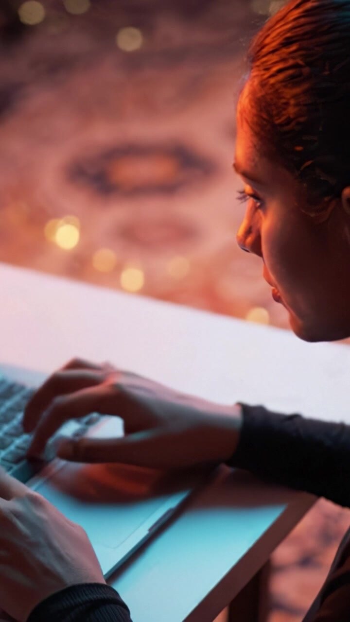 A focused individual engages with a laptop, immersed in work or study, highlighting dedication and concentration in a warm, softly lit environment.