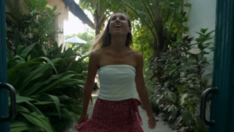 slow motion: young woman opens villa gate and walks into tropical garden.