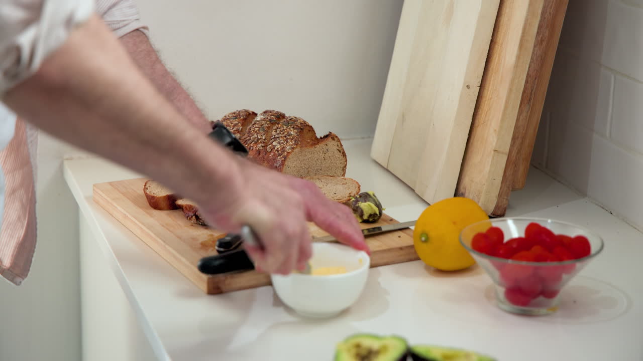 Senior man preparing fresh bread with butter and avocado in kitchen, at home