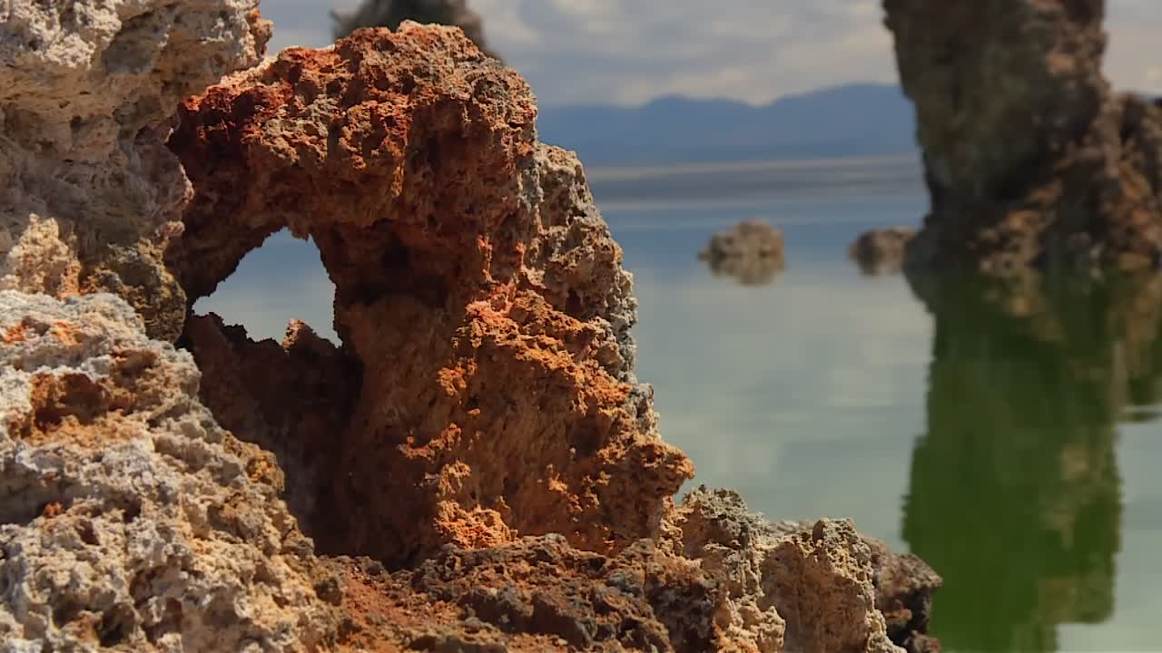 Roccia porosa di tufo color ruggine in primo piano nitido con una vista morbida sul lago e torri sullo sfondo, Lago Mono, California