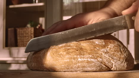 Hand-cutting-freshly-baked-homemade-wheat-bread-with-knife,-close-up