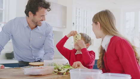 padre con hijos con uniforme escolar divirtiéndose haciendo sándwiches saludables para el almuerzo en casa