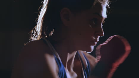 a beautiful woman boxer trains in a dark gym and works out punches in slow motion. camera movement side view. steadicam shot