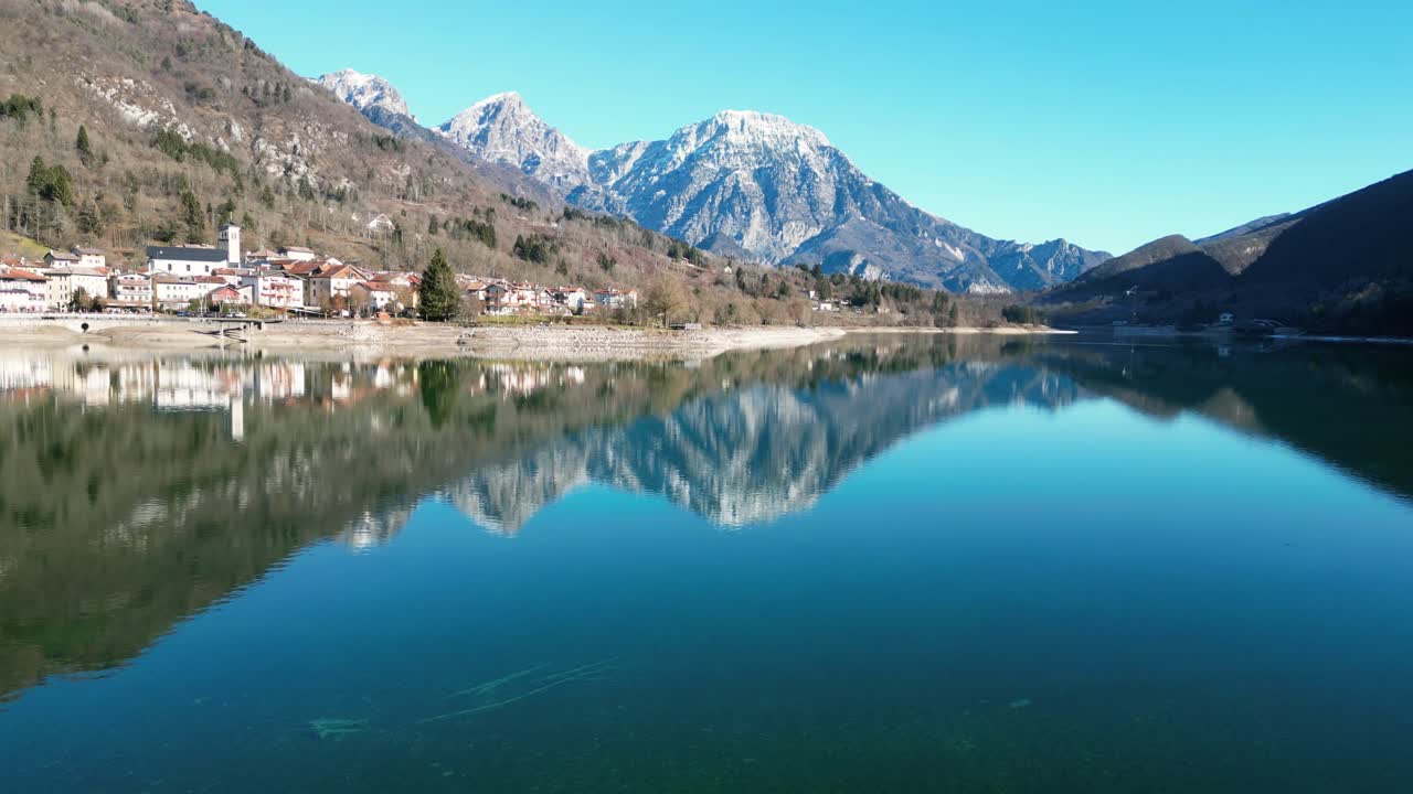 Rekaman drone udara Danau Barcis, Italia: hari musim dingin yang cerah, air berwarna pirus dan pegunungan, dengan puncak yang tertutup salju terlihat di kejauhan. Ideal untuk perjalanan, alam, dan rekaman stok yang indah