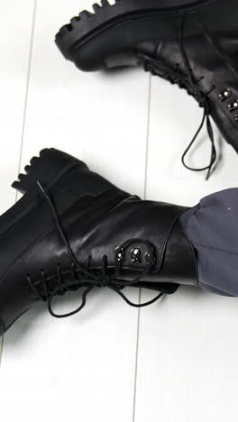 presentation of black leather stylish army boots with laces. modern sitting on the floor showing her modern footwear on tractor soles. vertical video