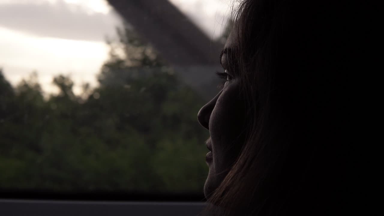 Close-up of woman's face looking to window in moving train. Darkened. Evening dusk. Side view