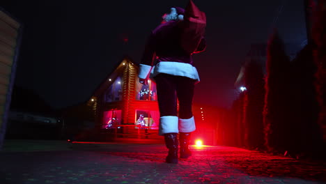 santa bringing gifts to kids. authentic santa claus carrying red bag over the shoulder and walking into the house. rear view.