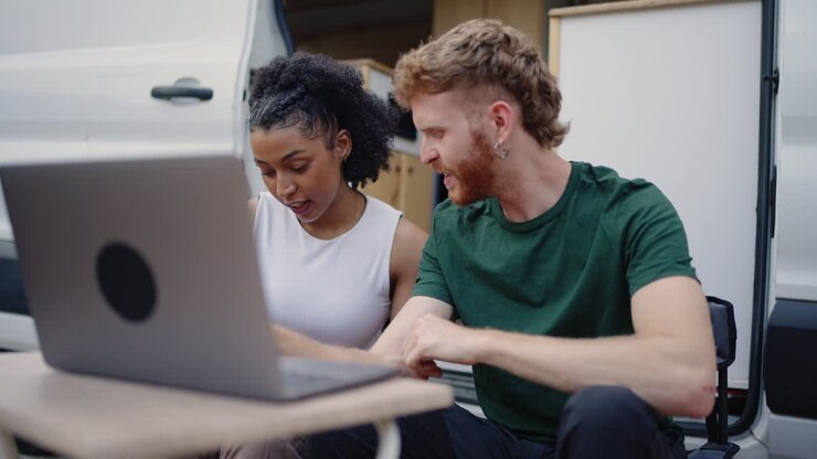 Couple working on laptop outside of campervan