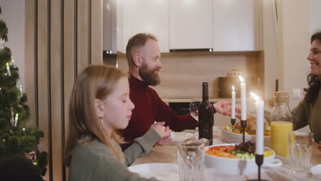 couple and their children pray and bless the table before christmas family dinner 3