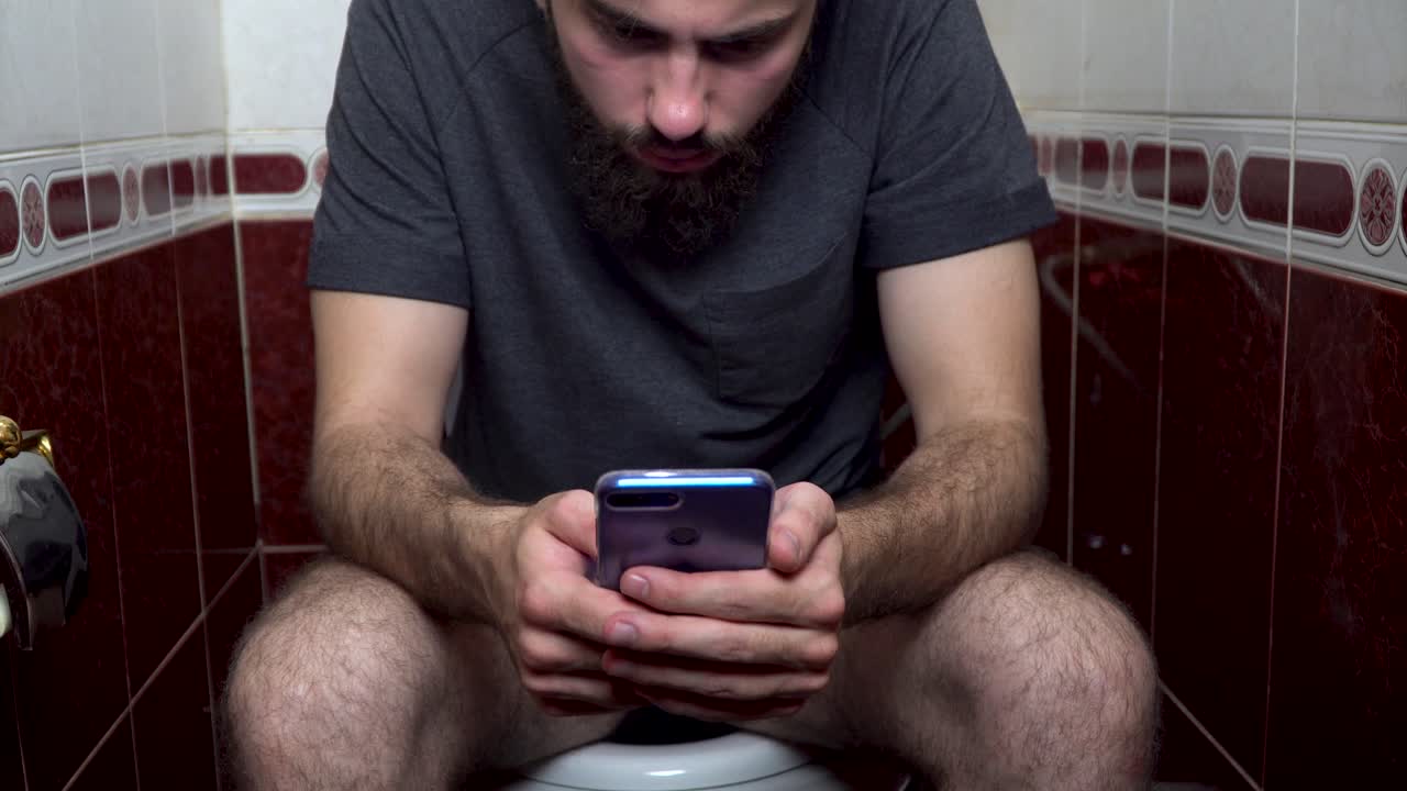 hombre usando un teléfono inteligente en un inodoro del baño