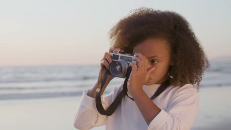 linda chica con cabello grueso y rizado tomando fotos con una cámara digital en la playa