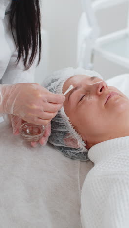 cosmetólogo aplicando ácido pelador hidratante en la piel alrededor de los ojos de la mujer tratamiento antienvejecimiento