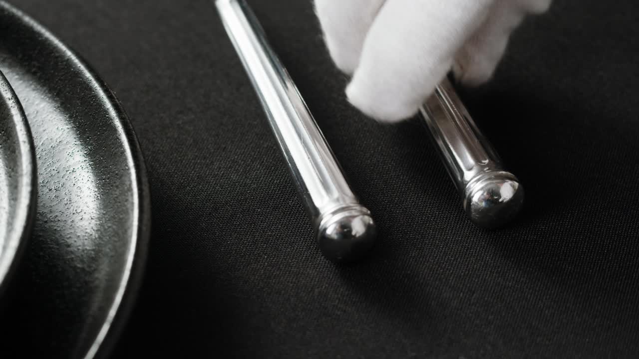 Professional table setting with white gloves. Plates, fork, knife, and glass arranged on a white table.