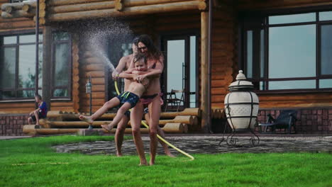 family in the backyard of a country house in the summer relax playing with water and hosing