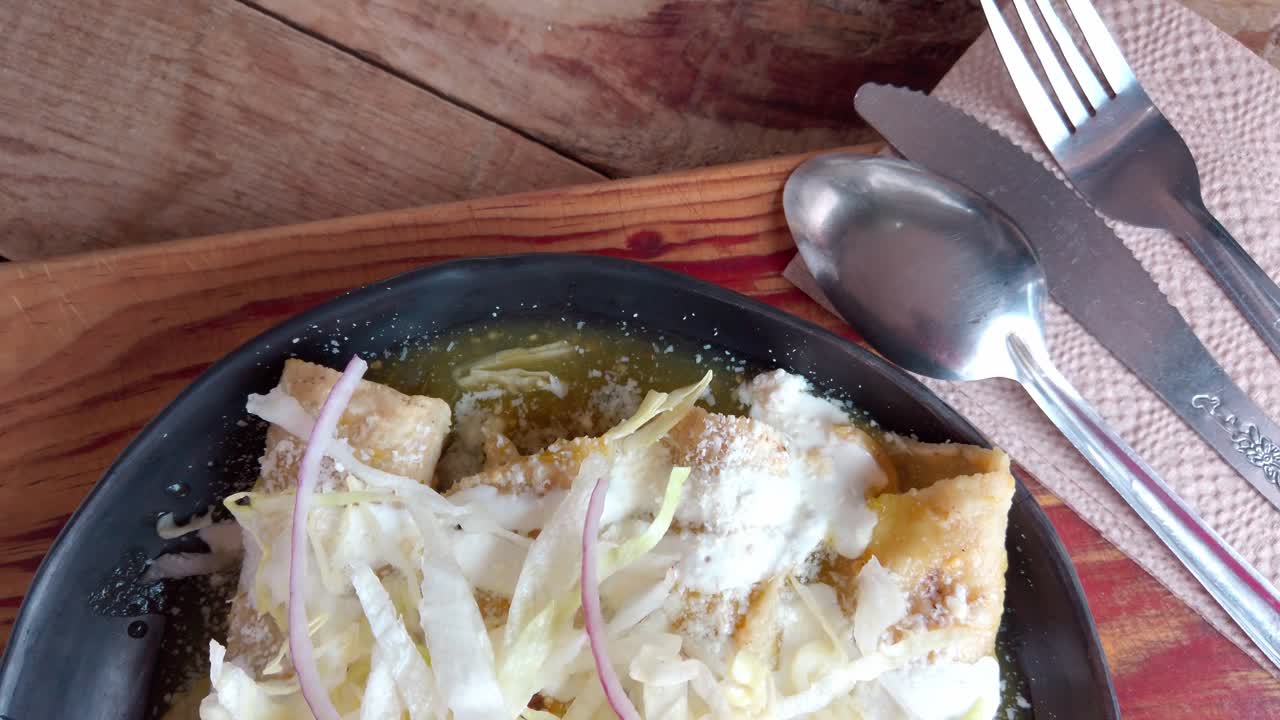 Crispy enchiladas with lettuce, onions, cheese, and green sauce, shot indoors