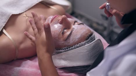 close up view of young woman lying on the couch while professional cosmetologist is applying special treatment on woman's face