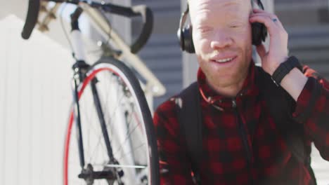 Happy-albino-african-american-man-with-dreadlocks-wearing-headphones-using-smartphone