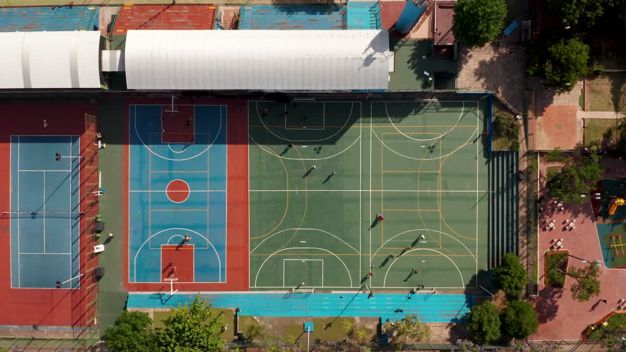 Vista superior de una cancha de baloncesto y campos de fútbol con jugadores bajo el sol.
