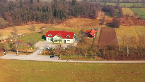 aerial shot arcing around a farmhouse while a person walks a dog along the road