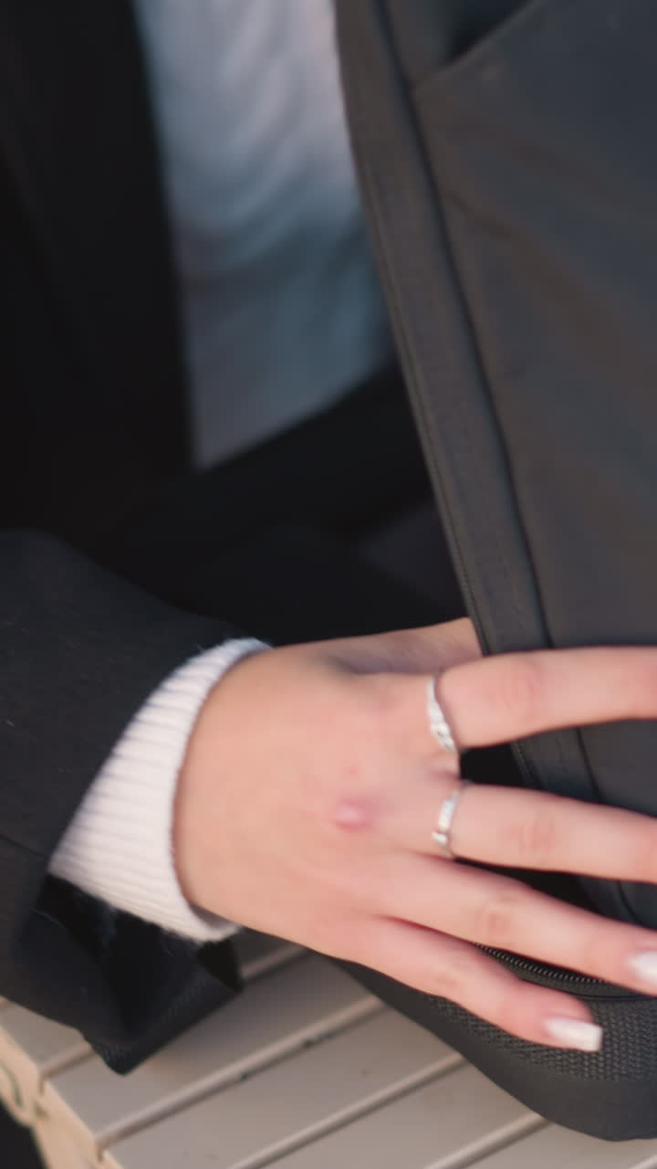 primer plano de una mujer con anillos y uñas pulidas abriendo una elegante bolsa negra en una mesa de madera y abriéndola para revelar una computadora portátil en el interior, en un entorno profesional y moderno