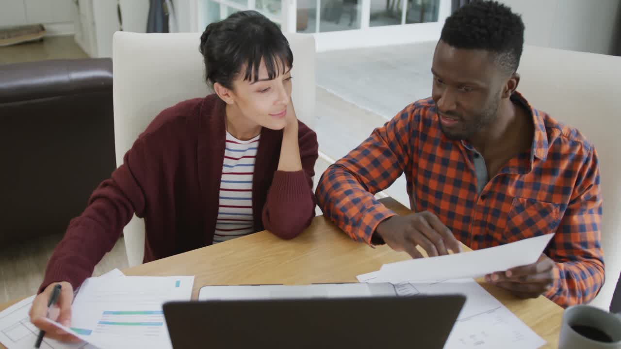 Happy diverse couple sitting at table and working with laptop