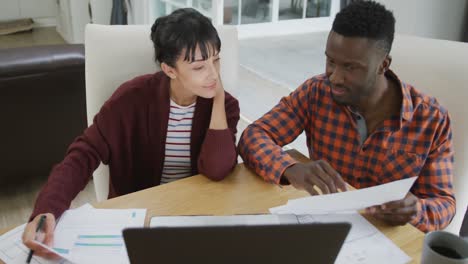 Happy-diverse-couple-sitting-at-table-and-working-with-laptop