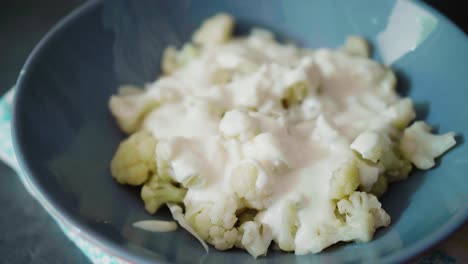 verter queso cremoso sobre coliflor cocida en un plato gris sobre fondo oscuro, alternativa saludable poco convencional a la comida tradicional eslovaca bryndzove halusky