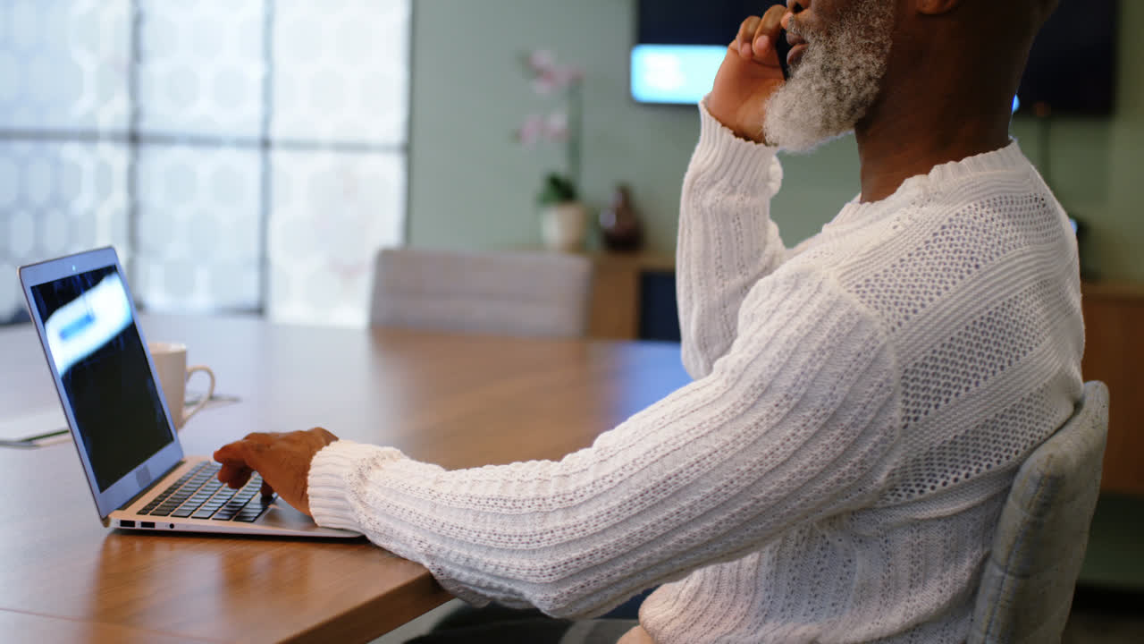 Uomo anziano che parla al telefono mentre usa il portatile 4k