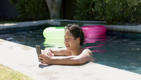 teenage asian boy enjoys a sunny day by the pool using a smartphone