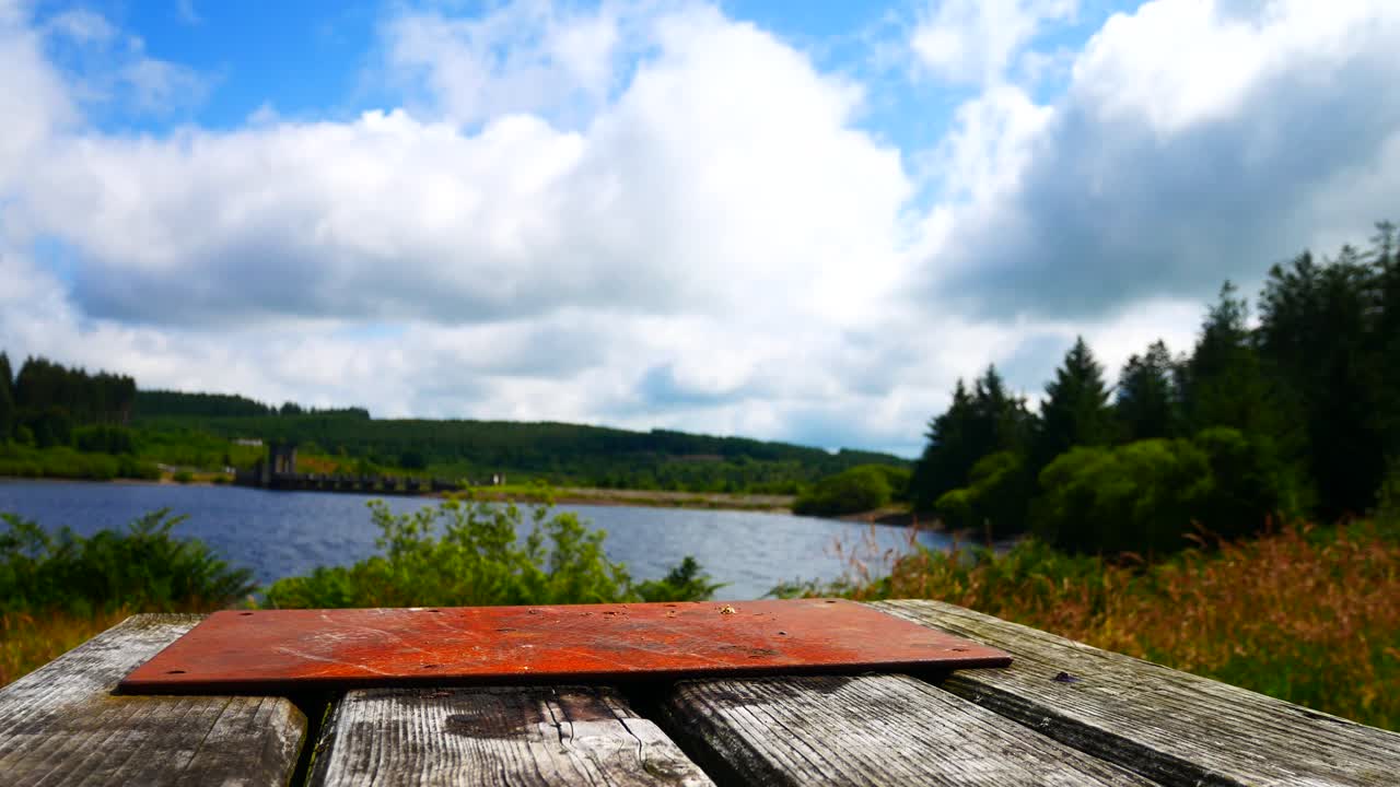 mesa de picnic de tablones de madera de ángulo bajo con vistas al cielo azul embalse escénico lago paisaje dolly izquierda