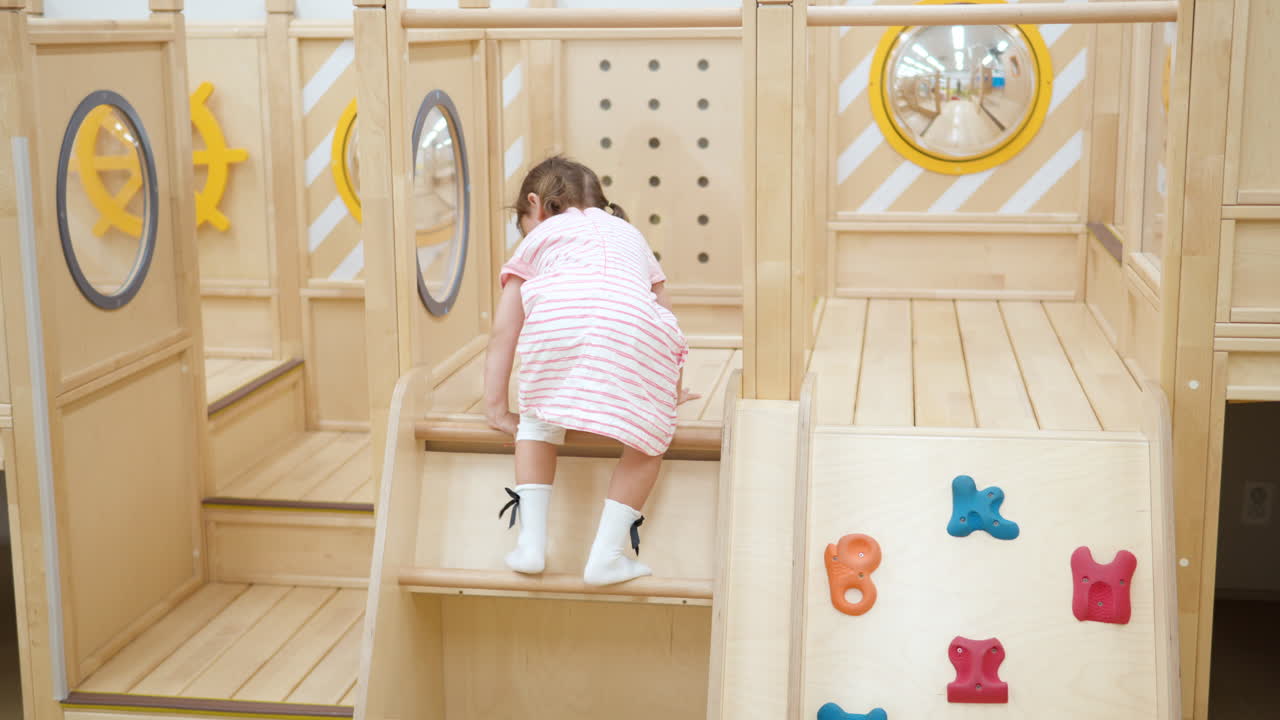 Aktives kleines Mädchen klettert und bewegt sich durch einen Hindernisparcours im Spielzimmer.